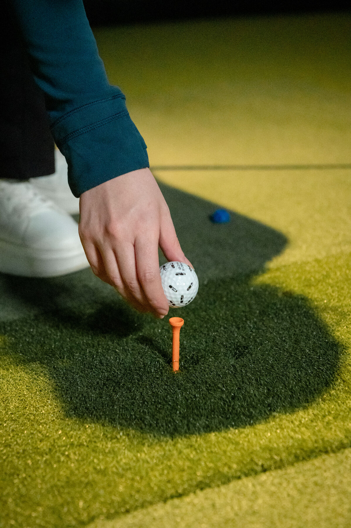 Close-up of a golfer setting a ball on an orange tee on the simulator turf at Digital Golf Fort Erie.