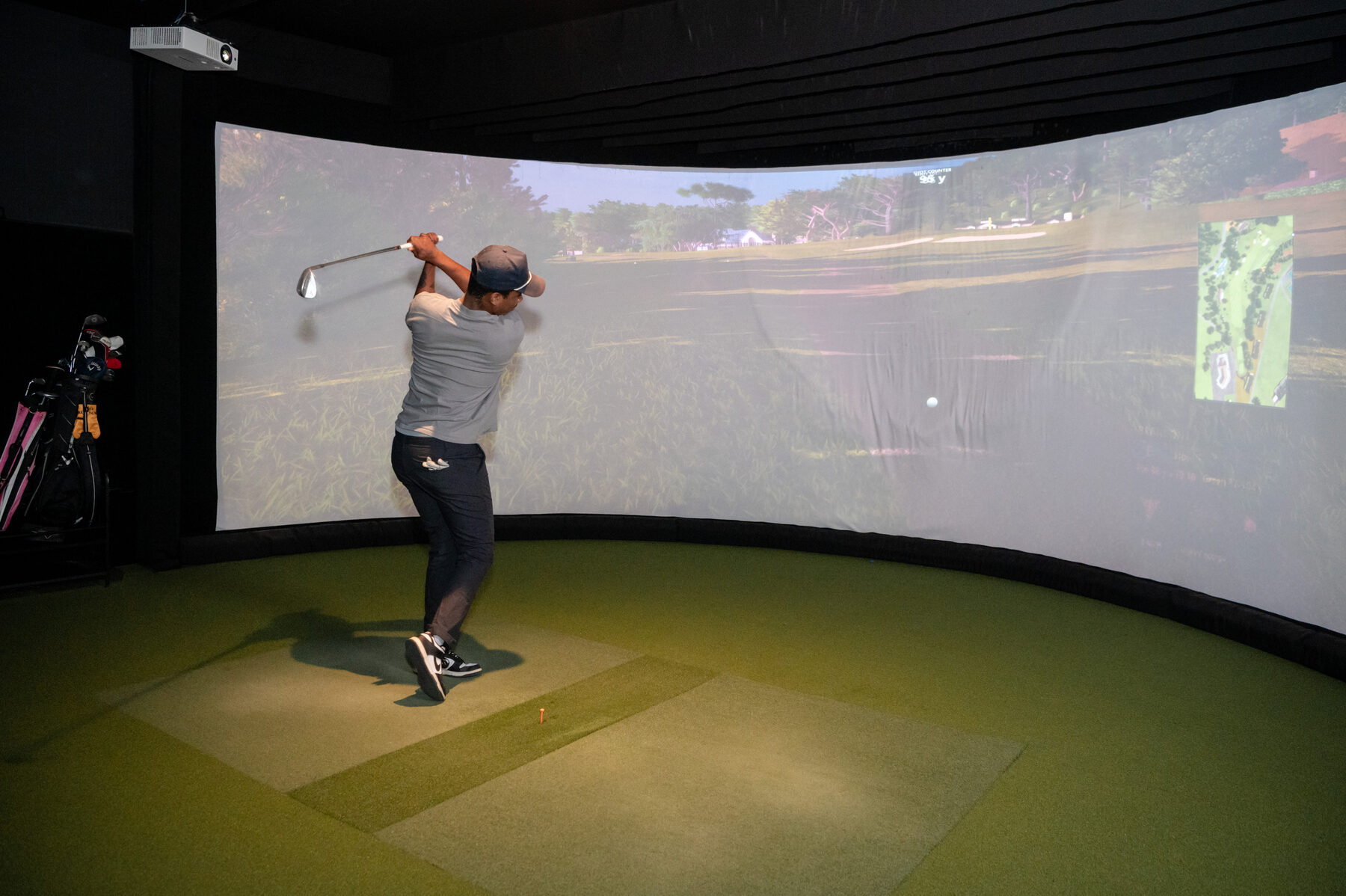 A golfer mid-swing in an indoor simulator bay at Digital Golf Fort Erie, with a fairway projected on the screen.